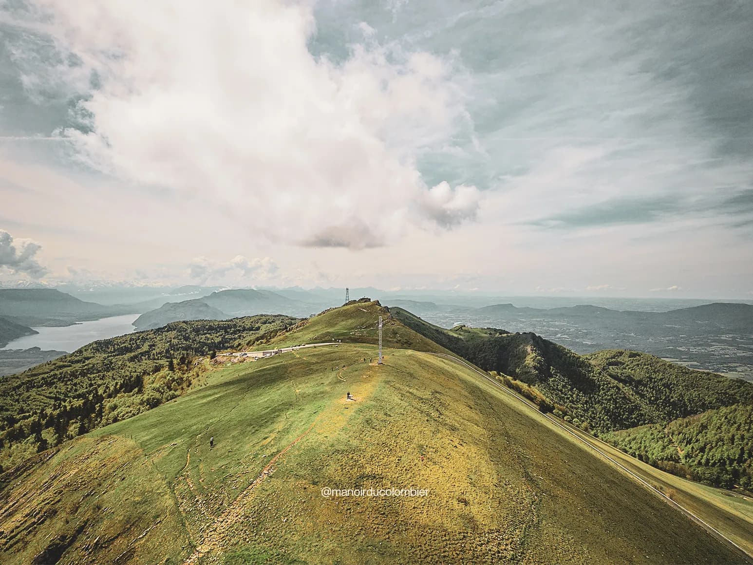 Vue panoramique du sommet du Grand Colombier, avec verdure, lac scintillant et montagnes environnantes.