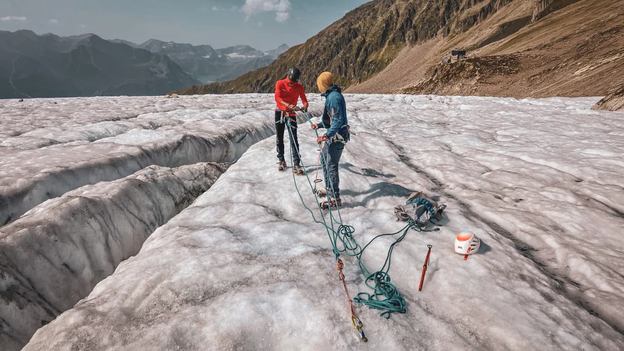 Deux alpinistes s'initient sur un glacier, entourés de paysages majestueux de montagnes.