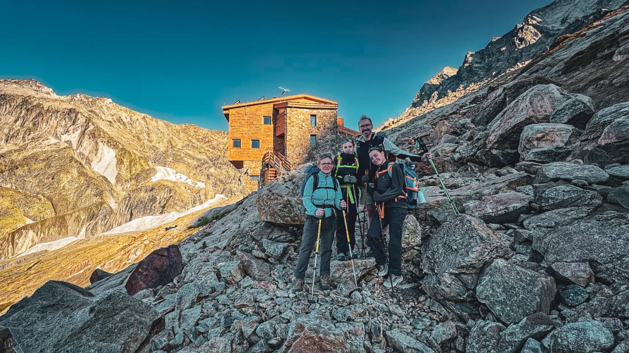 A group of hikers pose in front of an alpine Mountain hut, surrounded by breathtaking mountain scenery.