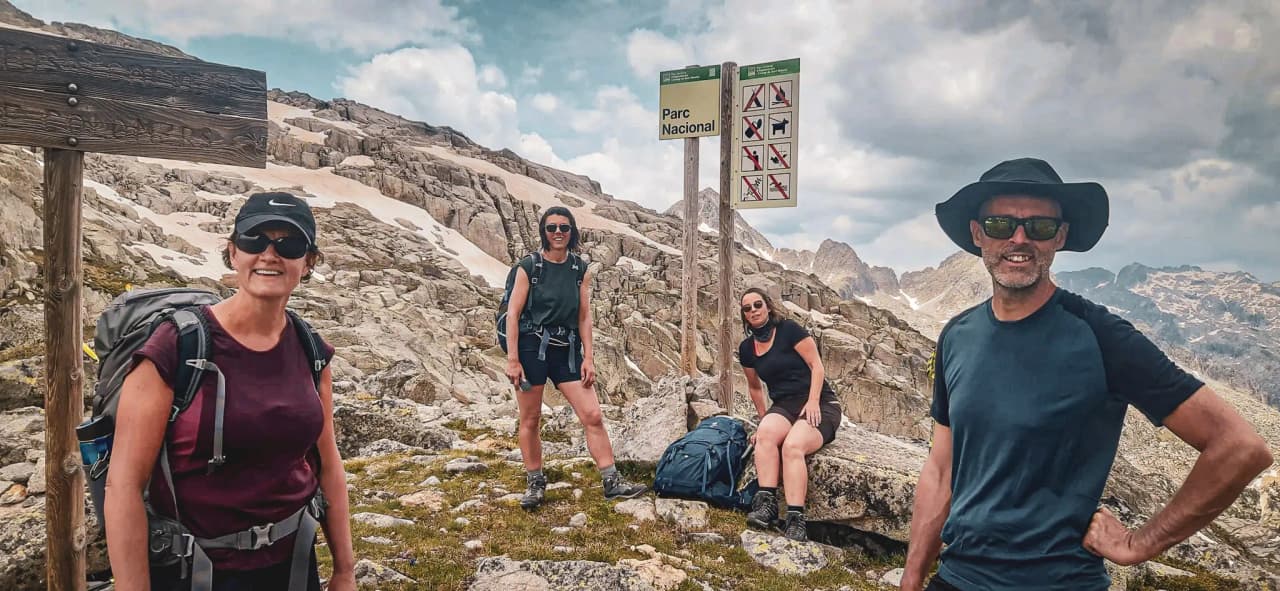 Four smiling hikers in the mountains, in front of a National Park sign, spectacular scenery.