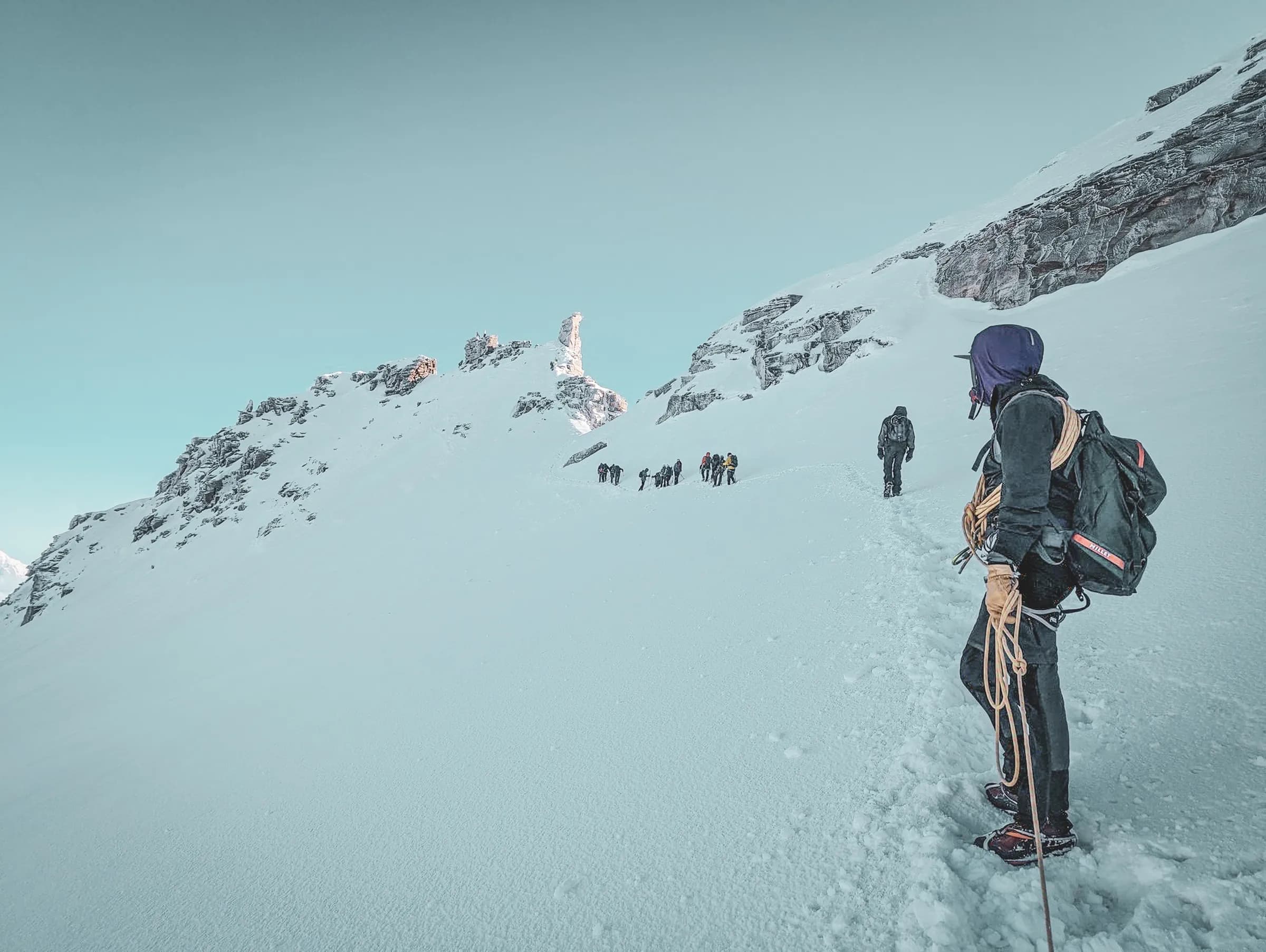 Group of climbers on their way to the snow-covered summit, majestic landscape and clear blue sky.