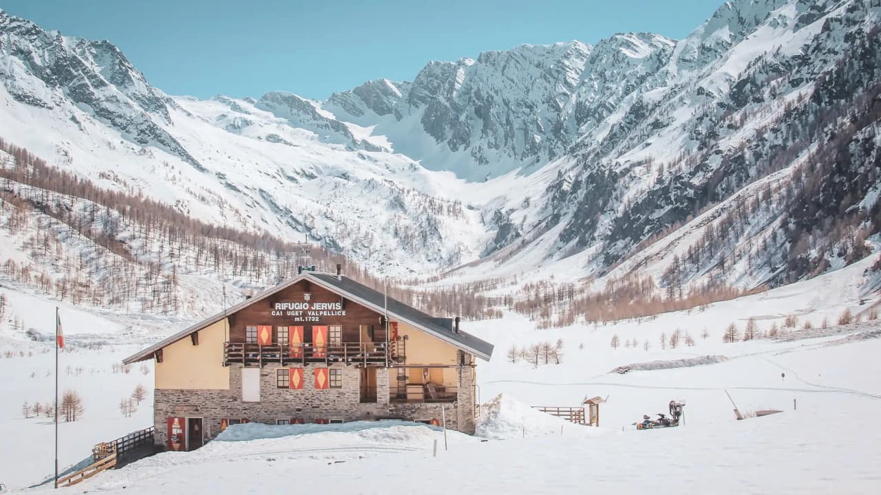 Picturesque mountain hut surrounded by snow-capped peaks in the Italian Alps.