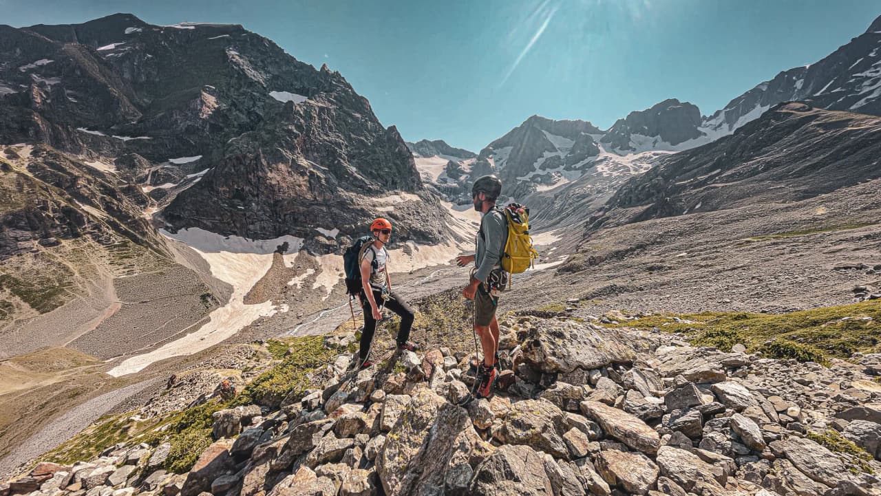Deux alpinistes discutent parmi des rochers, avec les majestueuses montagnes des Écrins en arrière-plan.