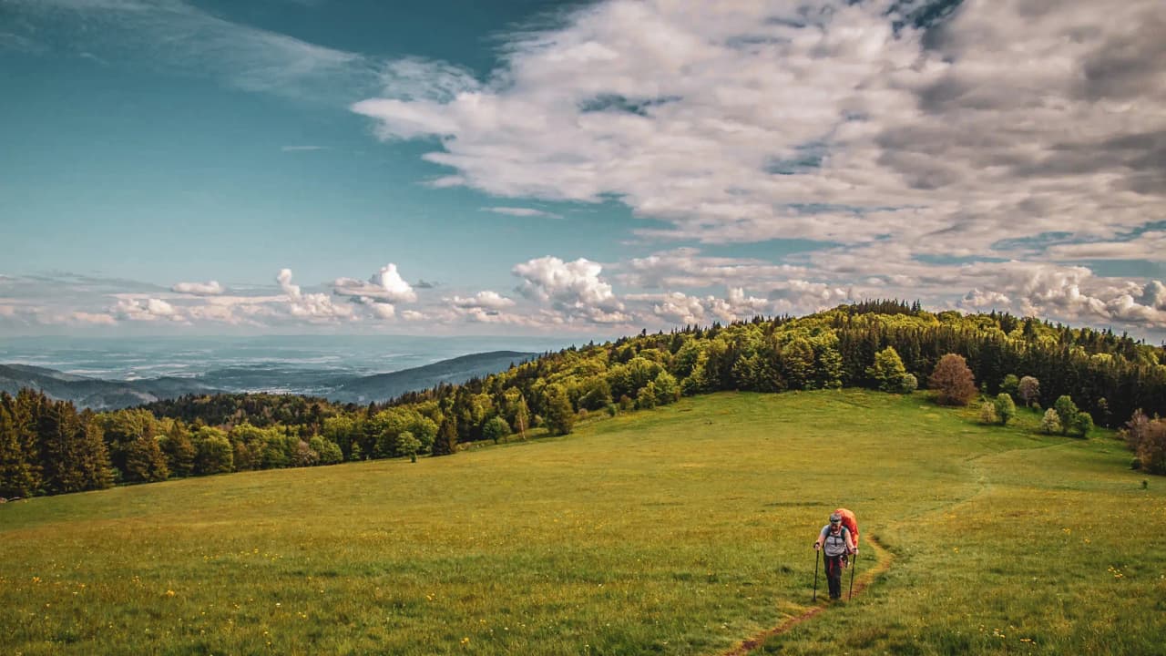 Randonneurs sur un sentier verdoyant, entourés de montagnes et de nuages, dans les Vosges.
