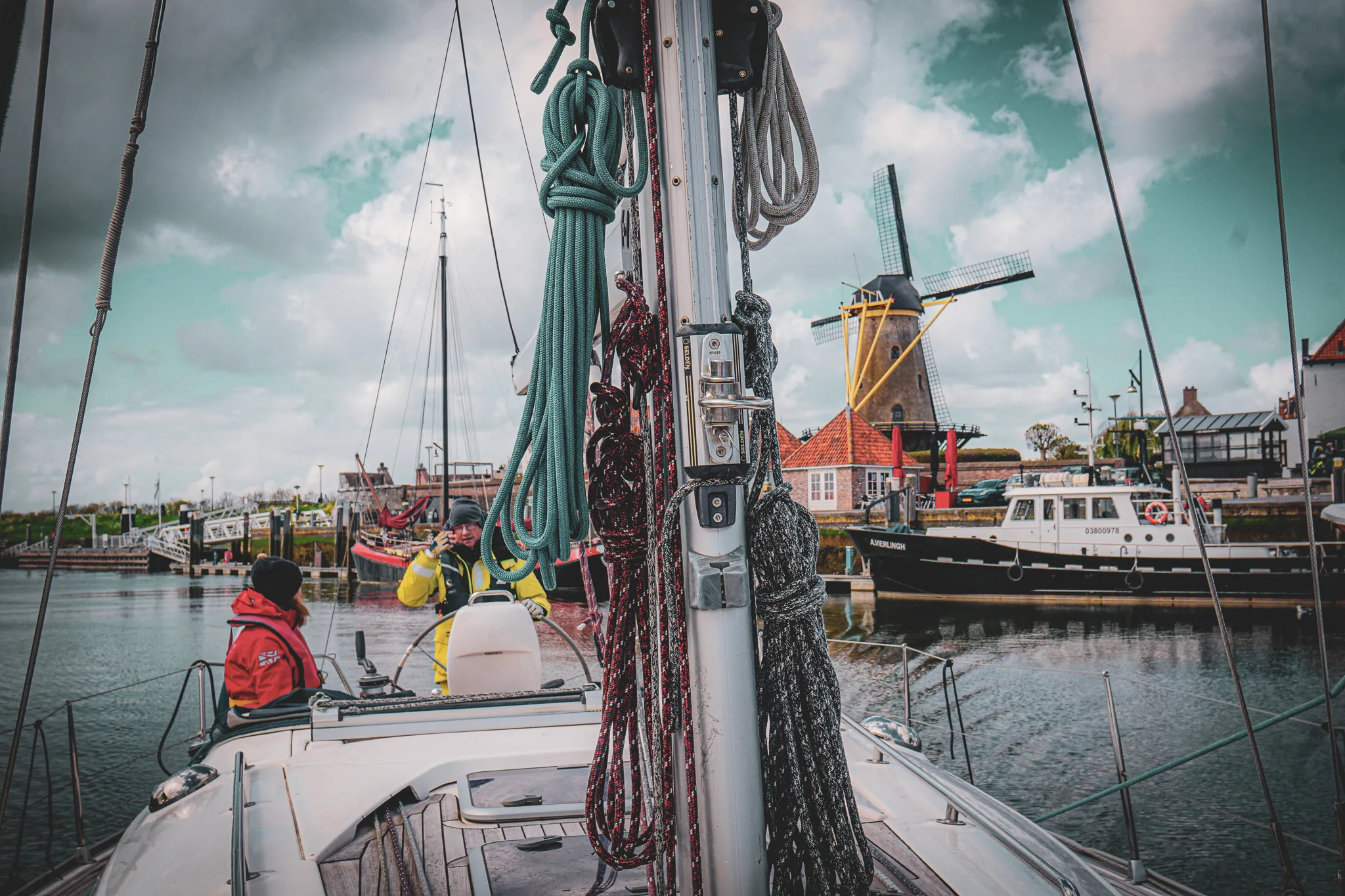 Une scène pittoresque en Zélande, avec un voilier, des quais animés et un moulin à vent.
