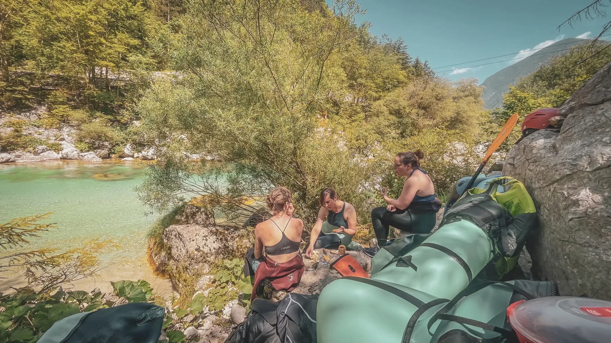 A group of travellers taking a break on the banks of a turquoise river, surrounded by greenery, ready for adventure.