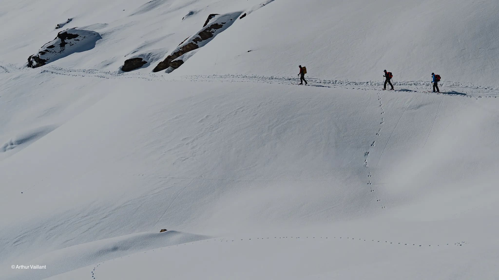 Two skiers are making their way across a vast expanse of pristine snow, surrounded by majestic mountains.