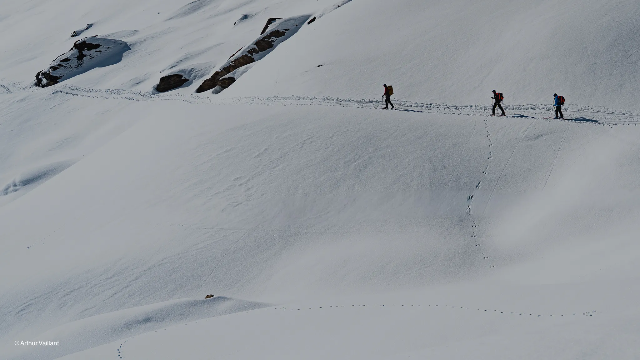 Two skiers are making their way across a vast expanse of pristine snow, surrounded by majestic mountains.