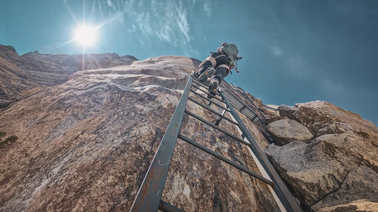 Een avonturier beklimt een ladder op een rotswand onder een stralend blauwe hemel.
