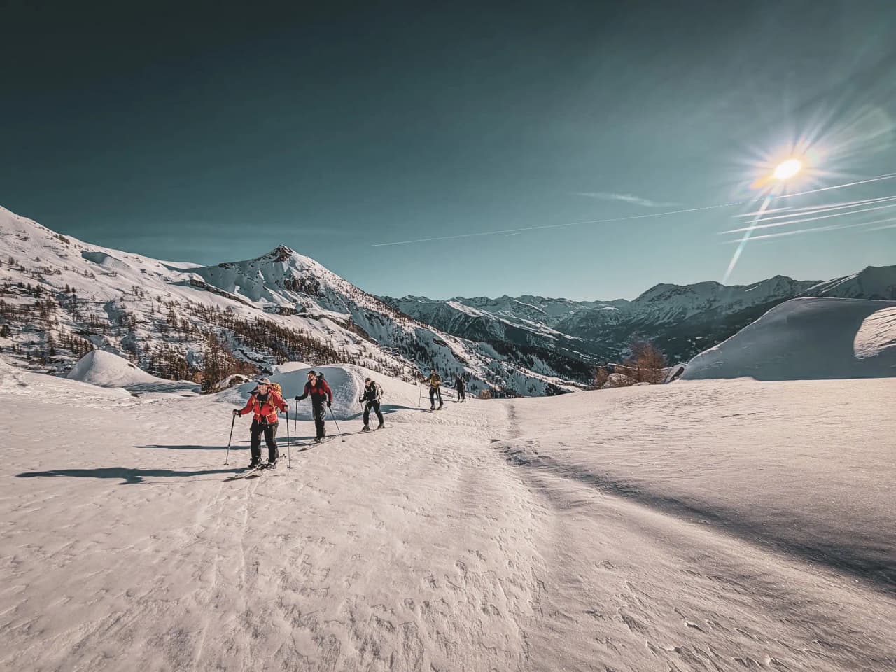 A group of ski tourers in a snow-covered landscape in the Écrins under a brilliant blue sky.