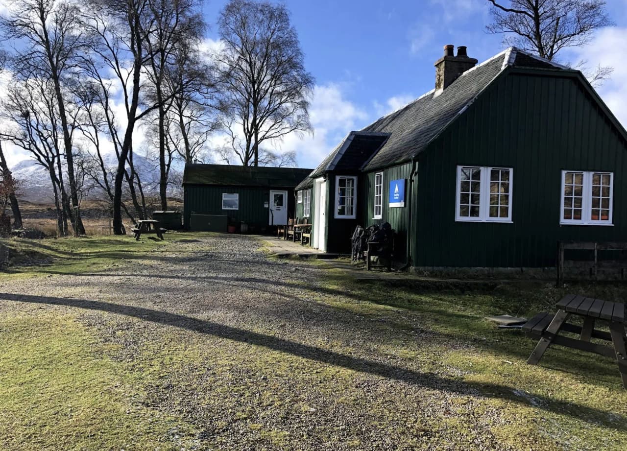 Een typisch groene hut in de Hooglanden, in een vredige omgeving omringd door bomen en blauwe luchten. Een uitnodiging voor avontuur!