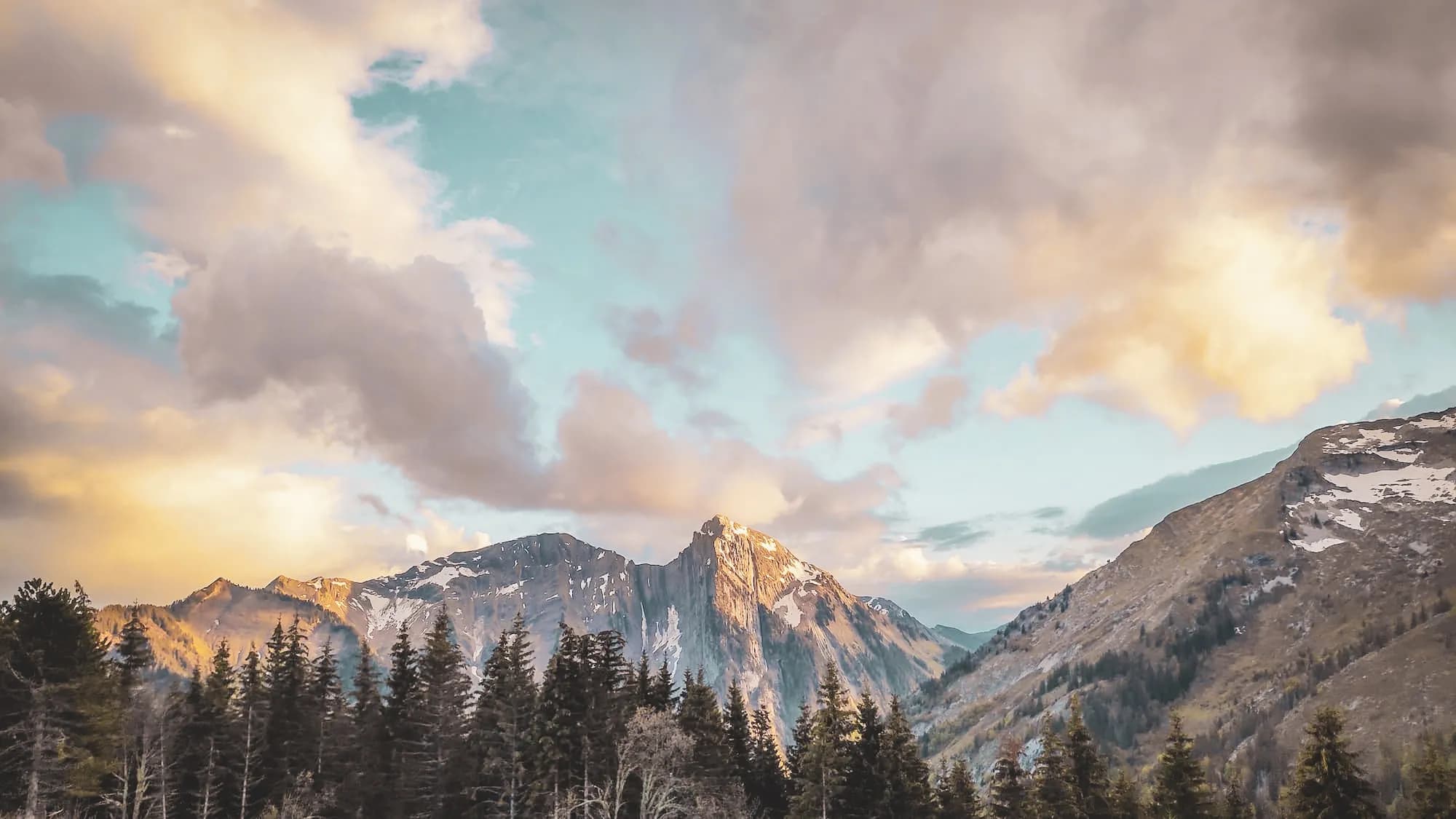 The mountain landscape of the Hautes Bauges, with sun-drenched peaks, lush green forests and vibrant skies.