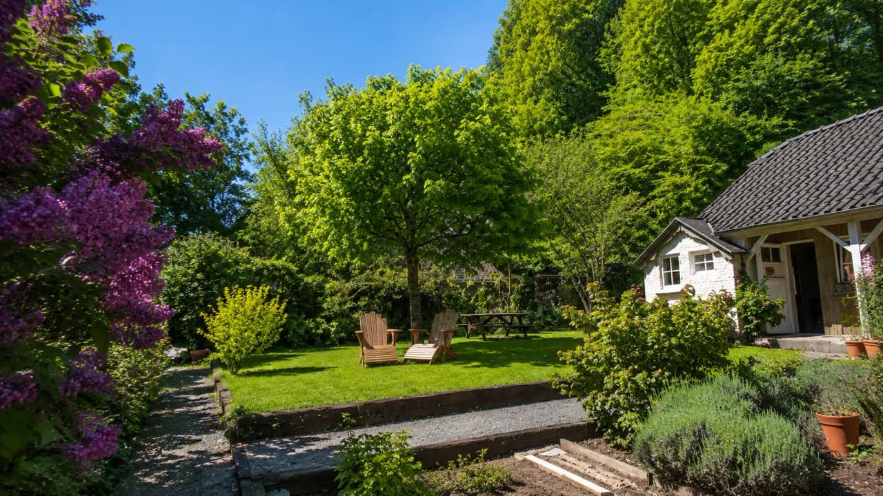 A green garden in Durbuy, with wooden armchairs under a blue sky, perfect for relaxing.