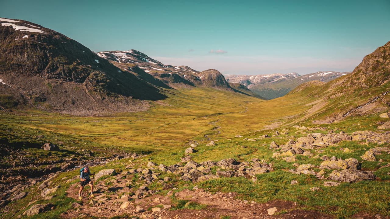 Hikers crossing a lush green valley, surrounded by majestic mountains. Escape guaranteed!