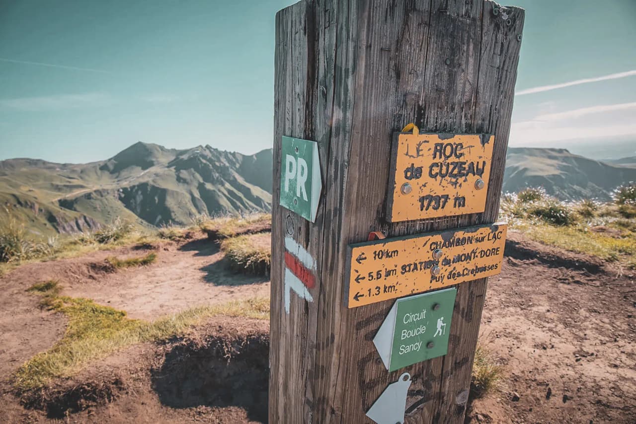 Wegwijzer op de top van de Roc de Cuzau, met majestueuze bergen op de achtergrond.