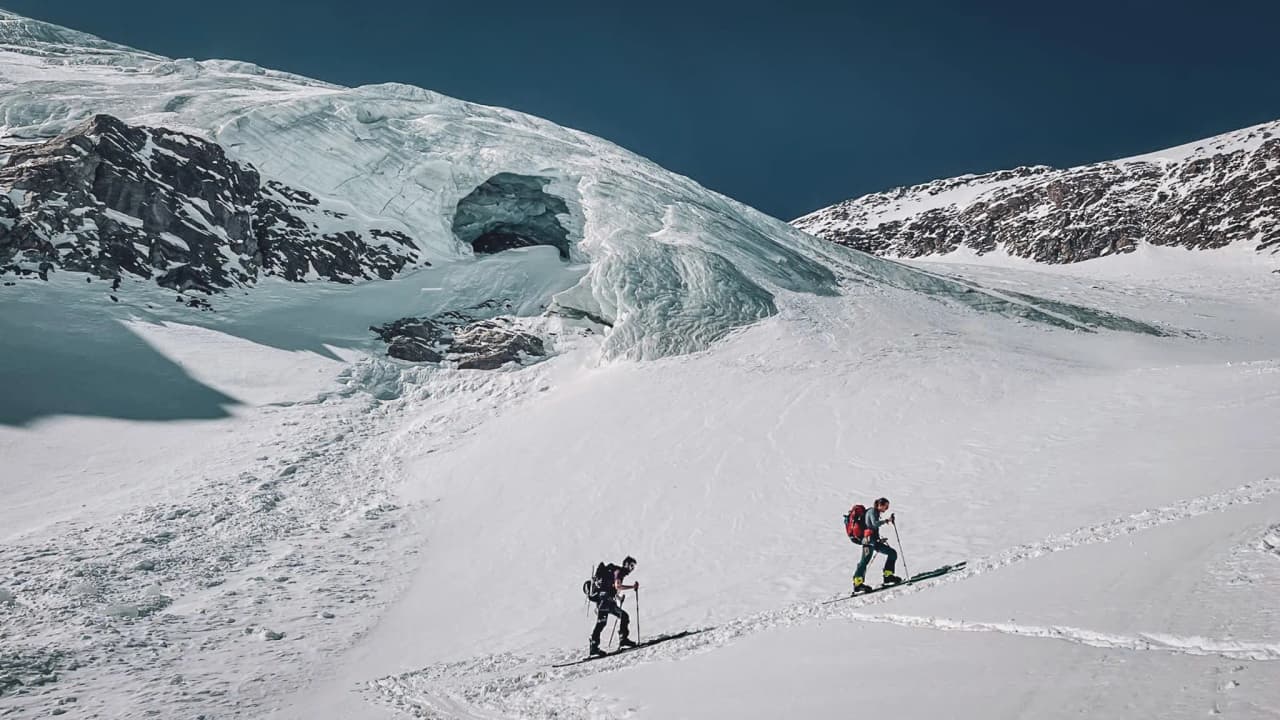 Two ski tourers make their way across a sparkling glacier, surrounded by majestic mountains.