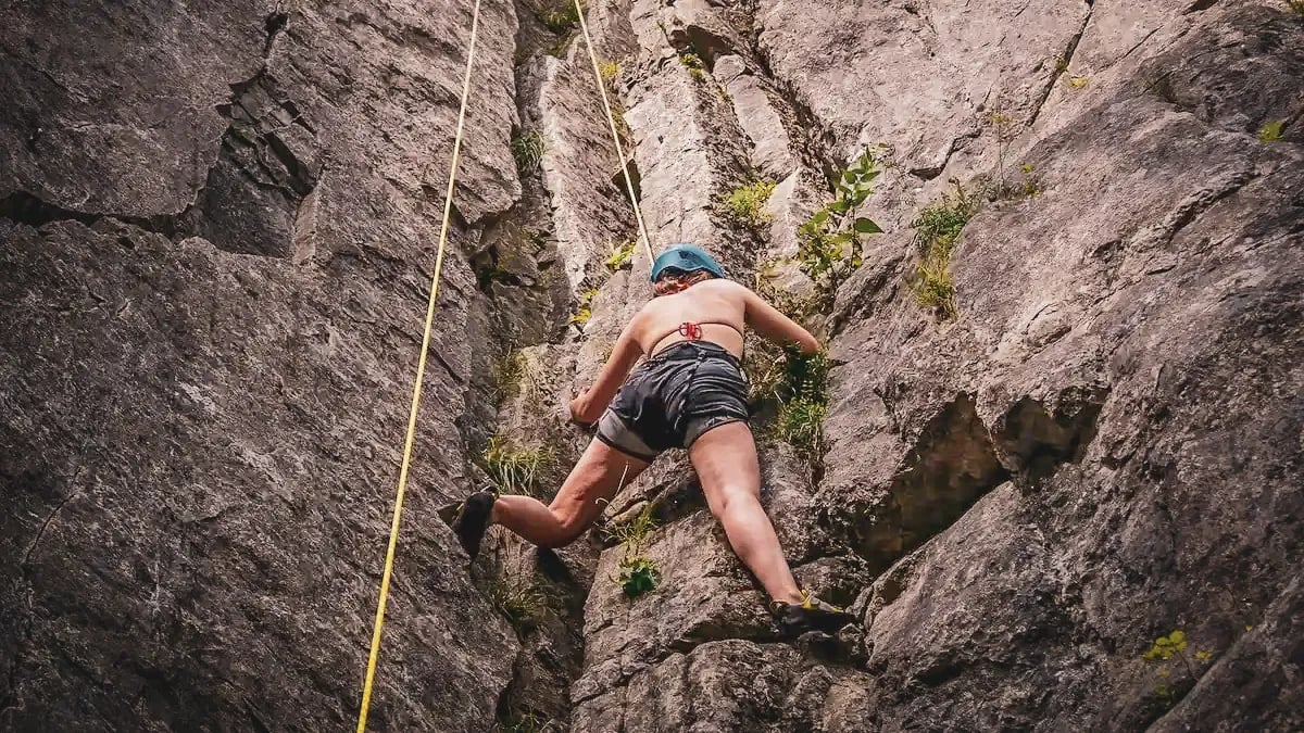 A climber tackles a green, rocky cliff, out in nature, in Belgium.