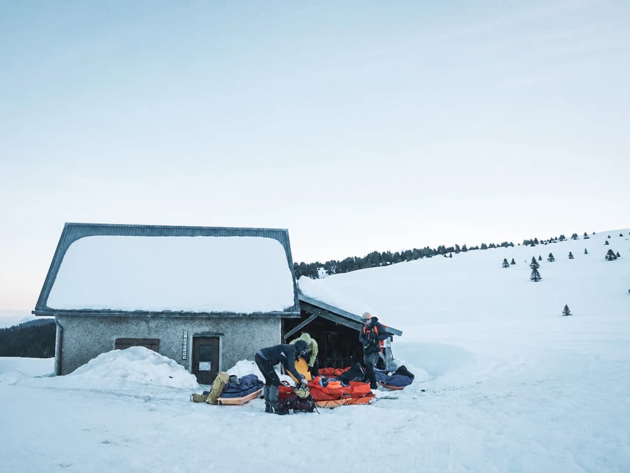 Een groep wandelaars die hun uitrusting klaarmaken bij een met sneeuw bedekte Berghut in de Vercors.
