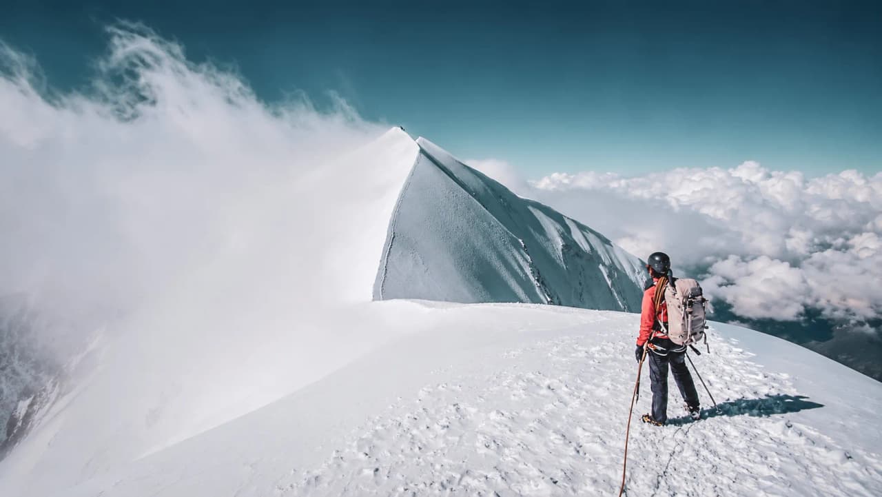 Een bergbeklimmer bekijkt de Dômes de Miage, omgeven door sneeuw en wolken, op de Mont Blanc.