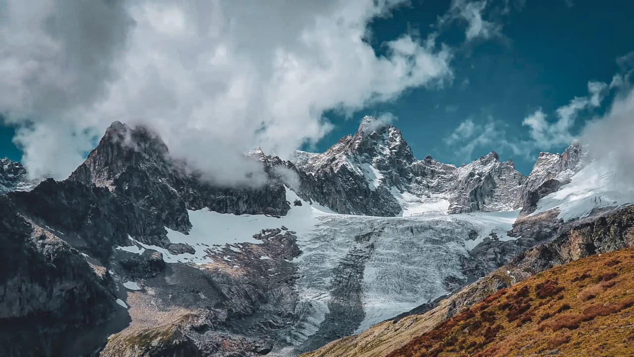 A spectacular panorama of snow-capped mountains under a blue sky dotted with clouds, an invitation to adventure.