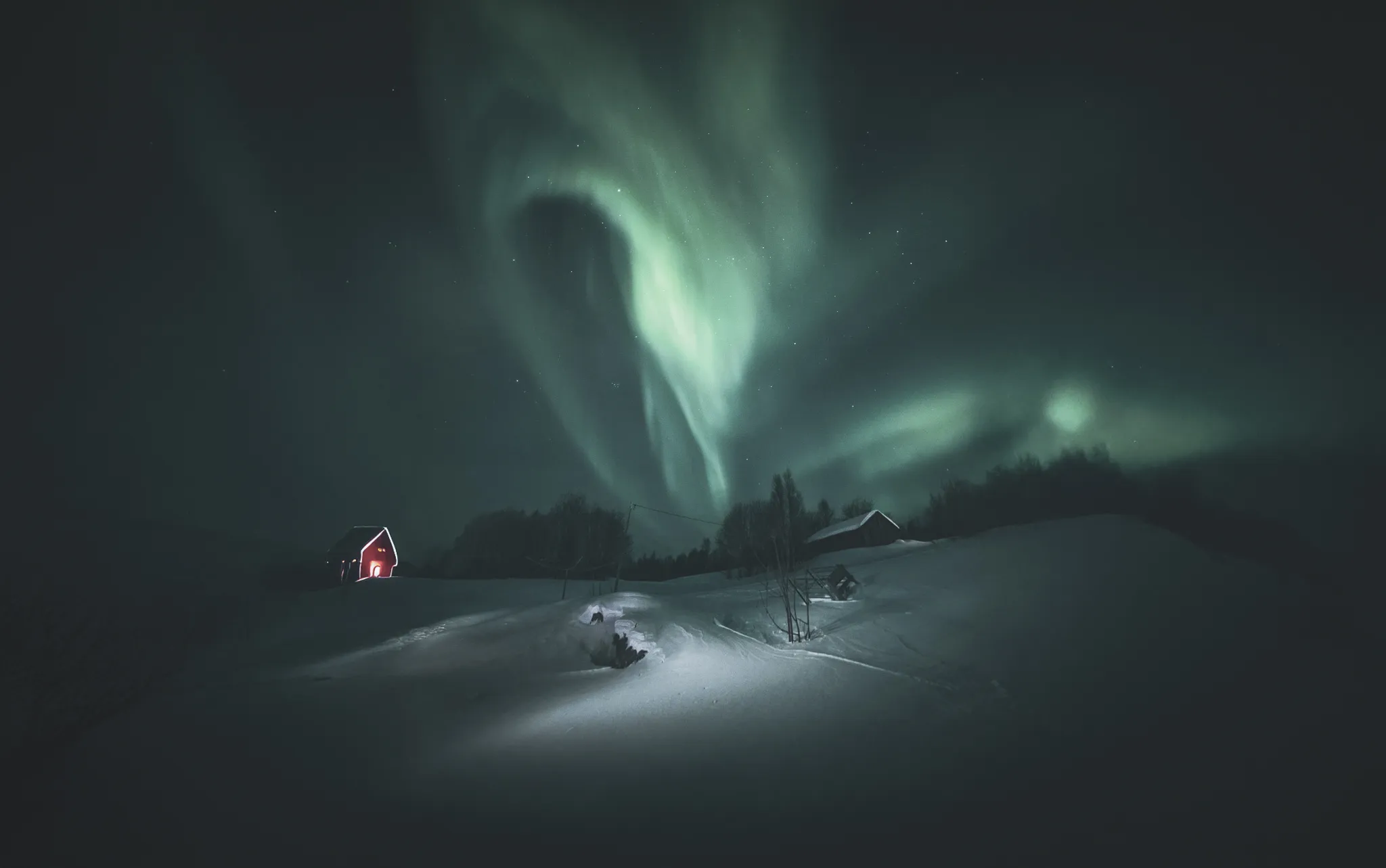Sublime aurora borealis illuminating a snow-covered landscape, with traditional houses in the background.