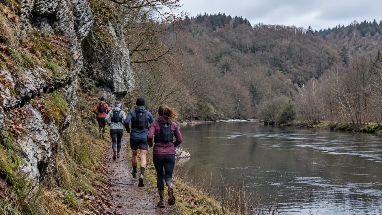 Un groupe de coureurs longe un sentier pittoresque au bord de la Semois, entouré de paysages sauvages.