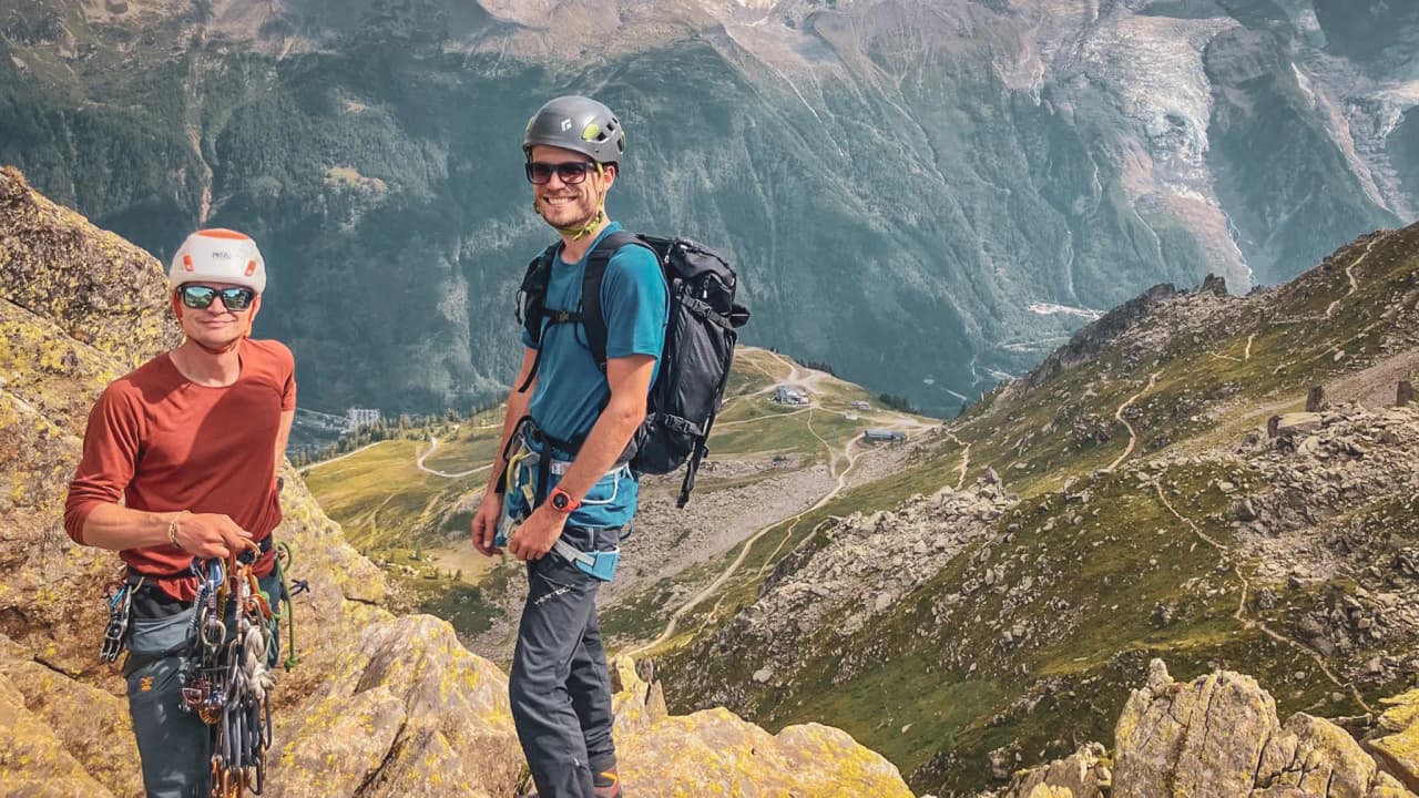 Deux alpinistes souriants sur les sommets de Chamonix, entourés de paysages majestueux.