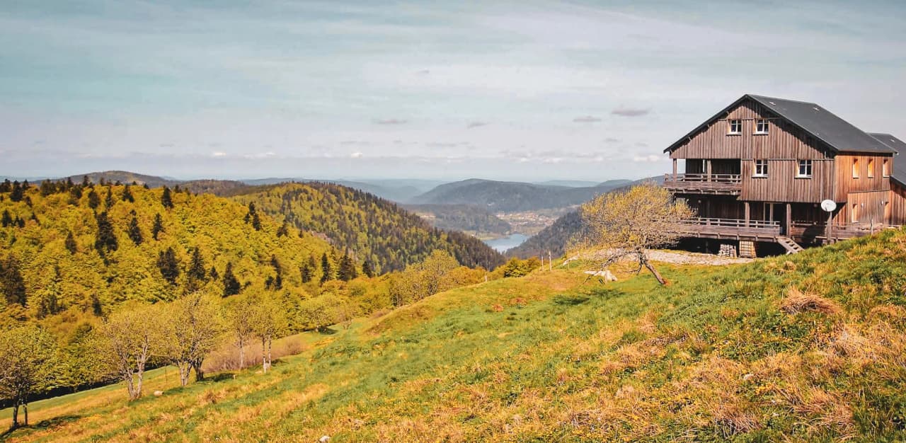 Un refuge en bois surplombant un panorama verdoyant des Vosges, idéal pour l'aventure en montagne.