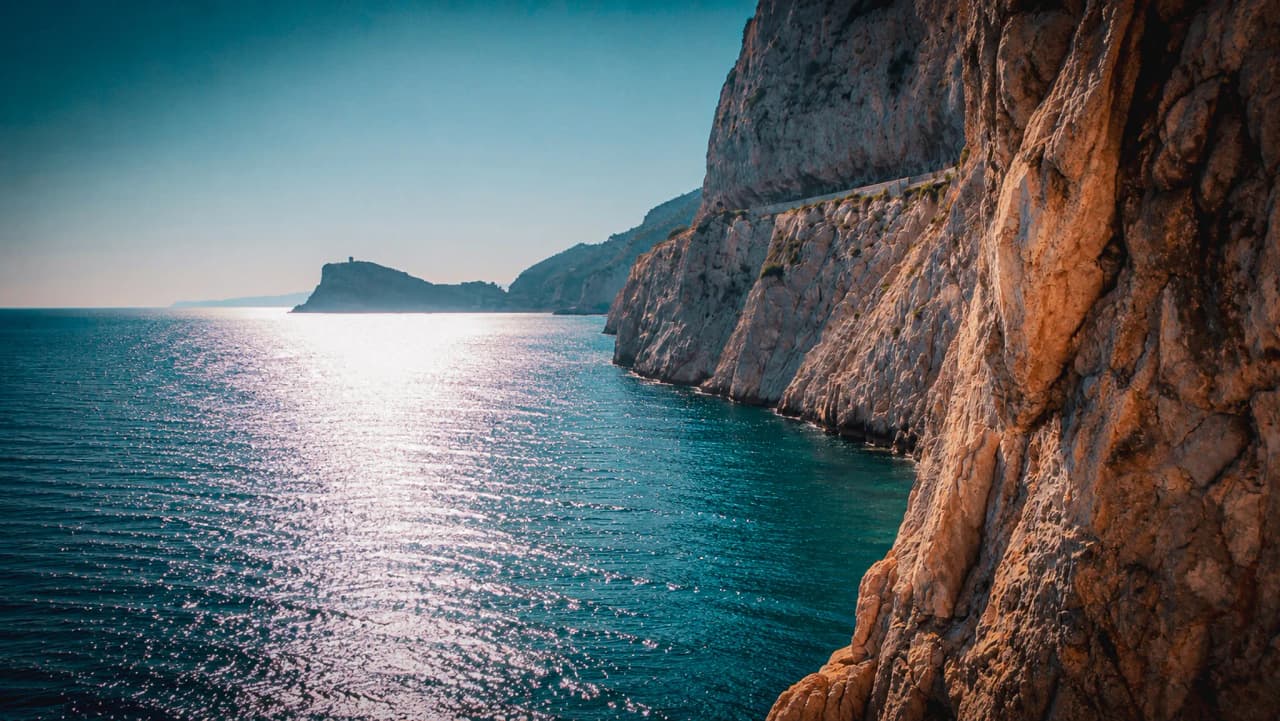 The sun-drenched Mediterranean coast, with glistening reflections on the water and majestic cliffs.