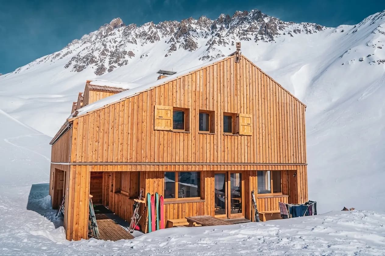 A cosy wooden Mountain hut surrounded by snow-capped mountains, ideal for a snowshoeing adventure.