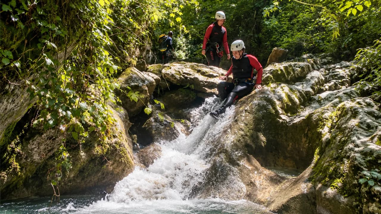 Des aventuriers s'élancent dans un canyon verdoyant, entre rochers et cascades rafraîchissantes.