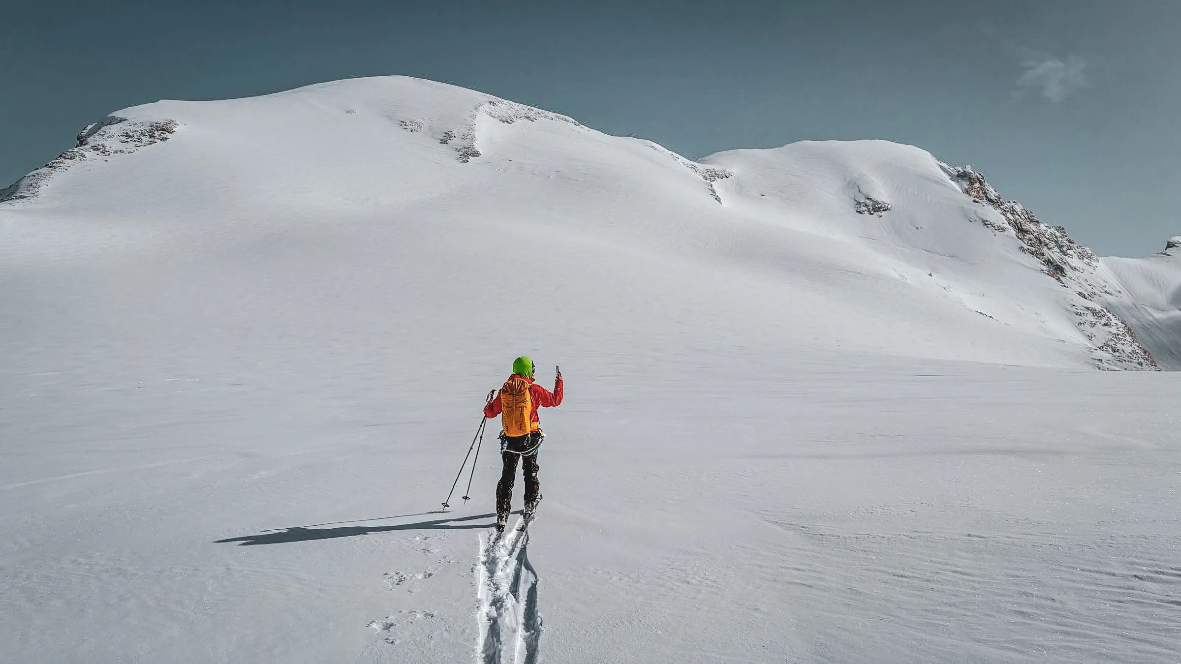 Skieur traversant un paysage alpin enneigé, entre sommets majestueux et glaciers étincelants.