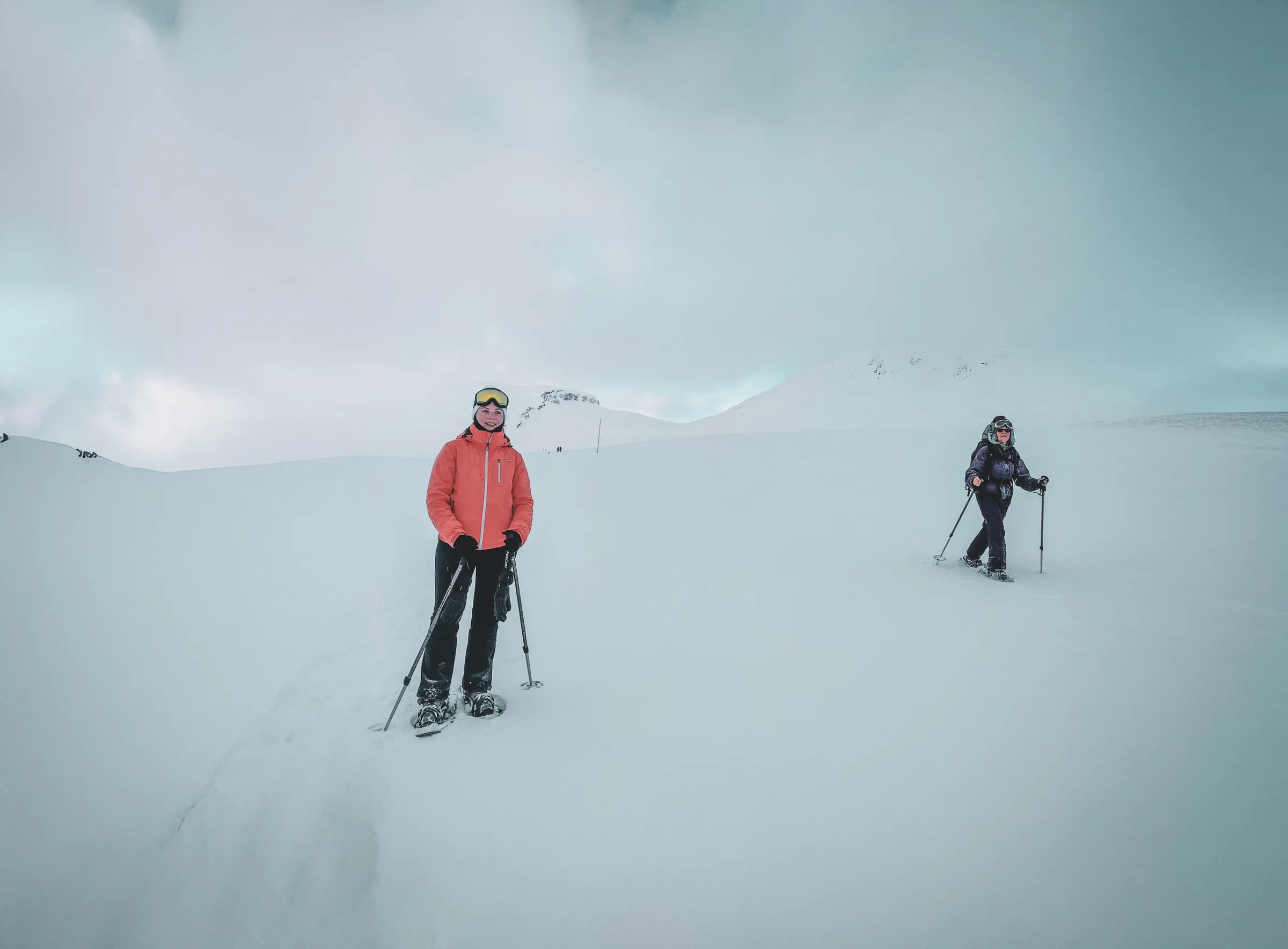 Two hikers on snowshoes, surrounded by sparkling snow, under a cloudy sky in Lapland.
