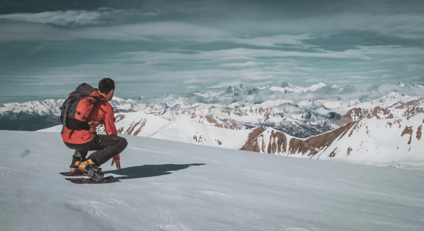 Snowshoe trekking on a snow-covered summit, admiring majestic Alpine scenery.