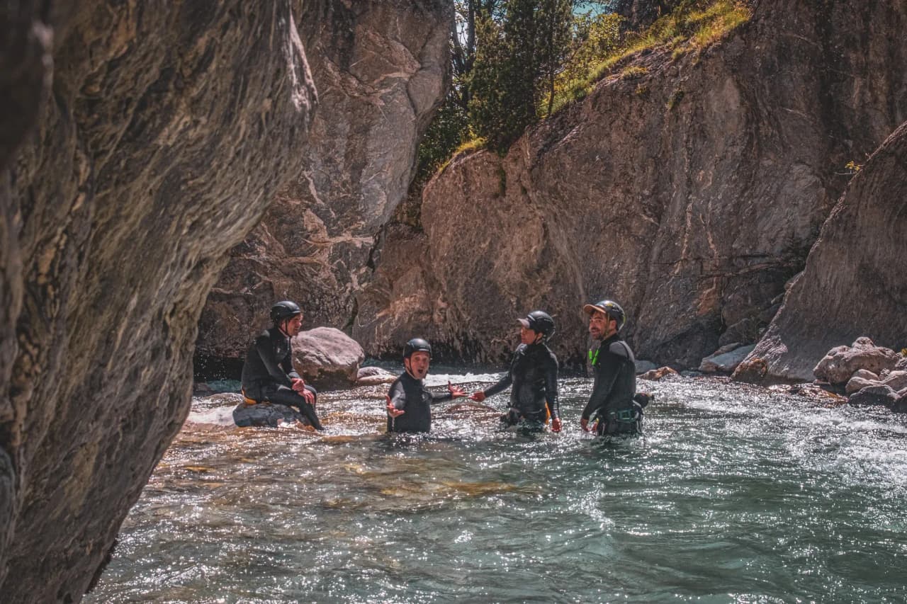 A group of wetsuit-clad adventurers enjoy an Alpine river surrounded by majestic cliffs.