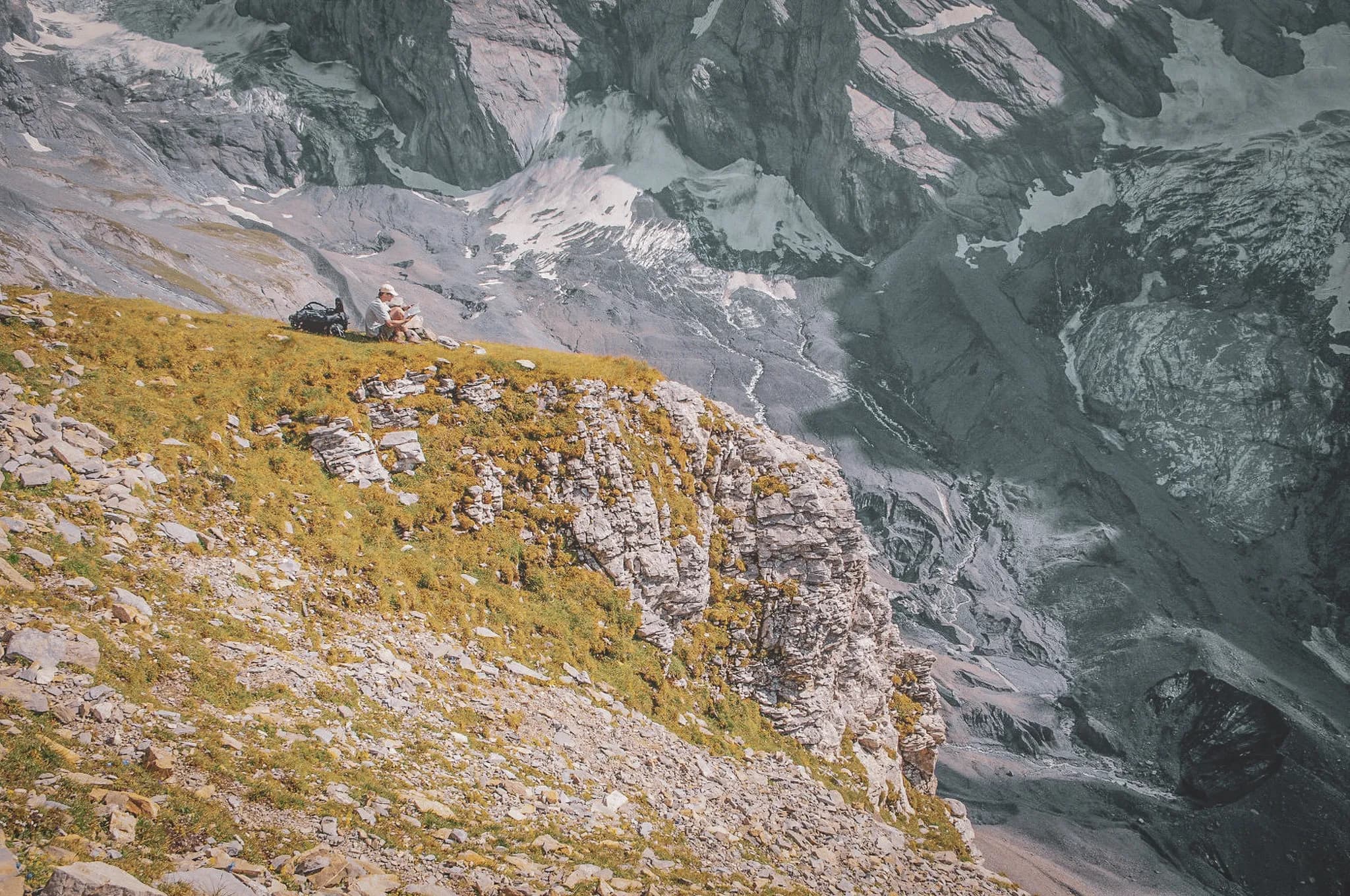 A hiker sitting on a green slope, admiring the majestic mountains and glaciers of the Alps.