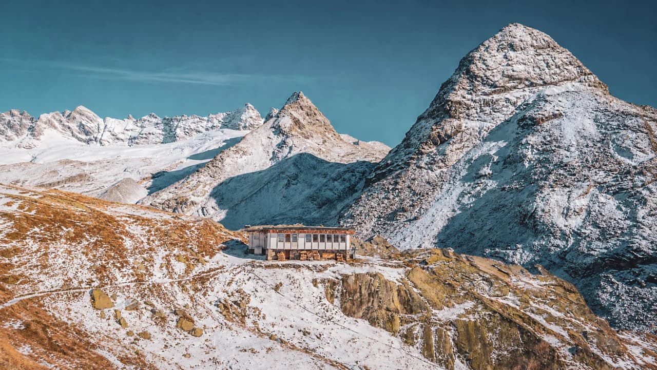 An alpine mountain hut nestled between snow-capped peaks, inviting you to embark on a wilderness adventure.