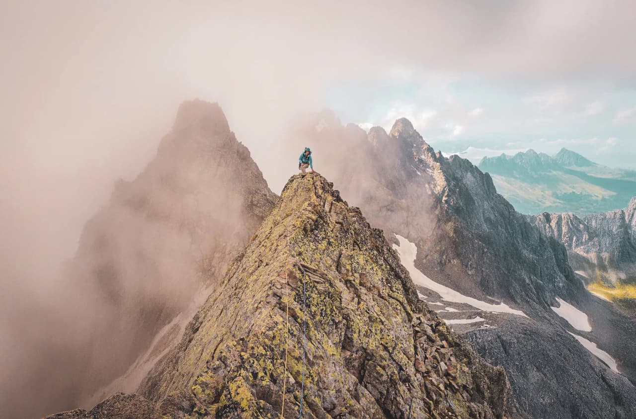 A hiker conquers a steep ridge, surrounded by majestic, misty landscapes.