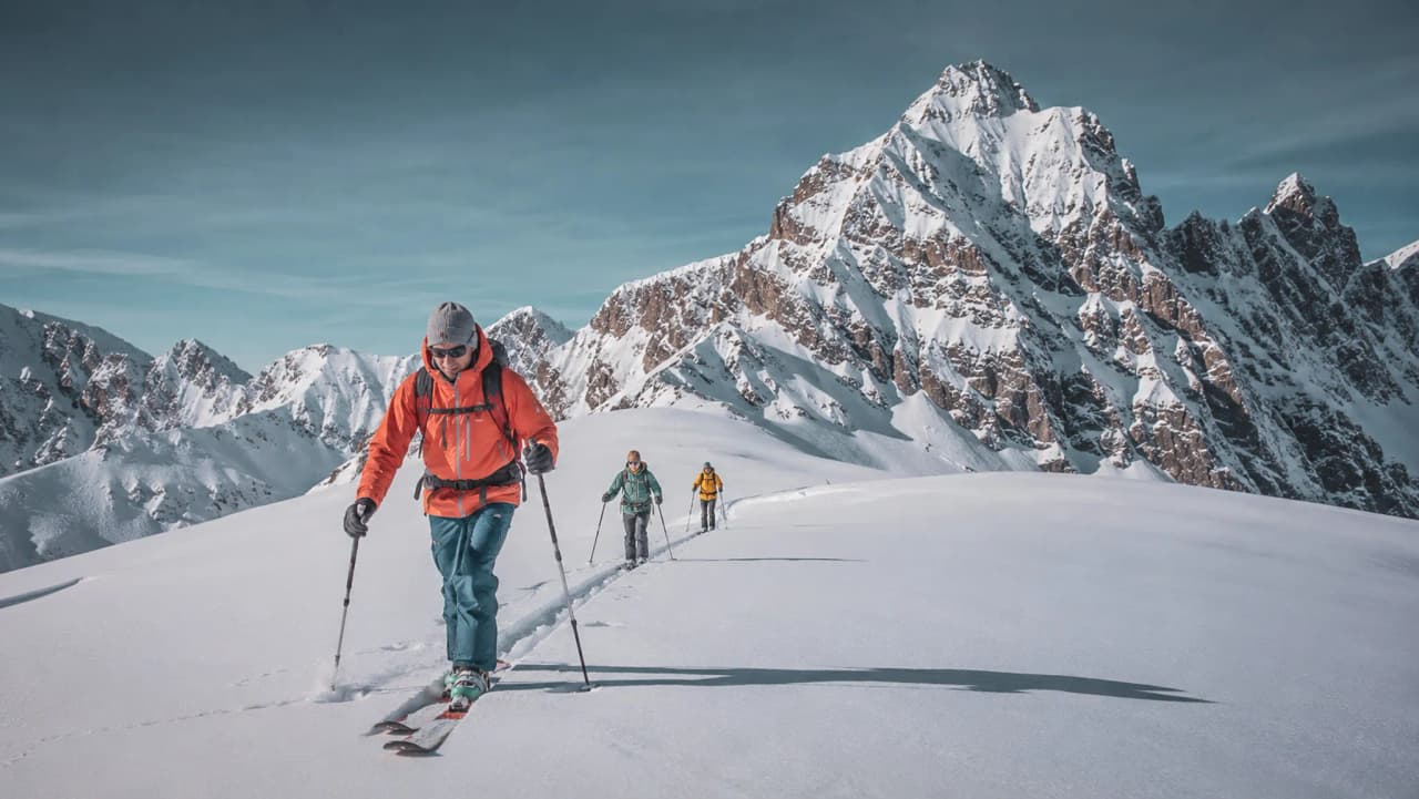 A group of ski tourers in a majestic alpine landscape, with pristine snow and magnificent peaks.