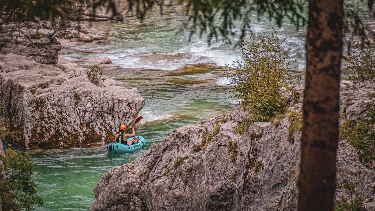 An adventurer glides peacefully down an alpine river, surrounded by rocks and greenery.