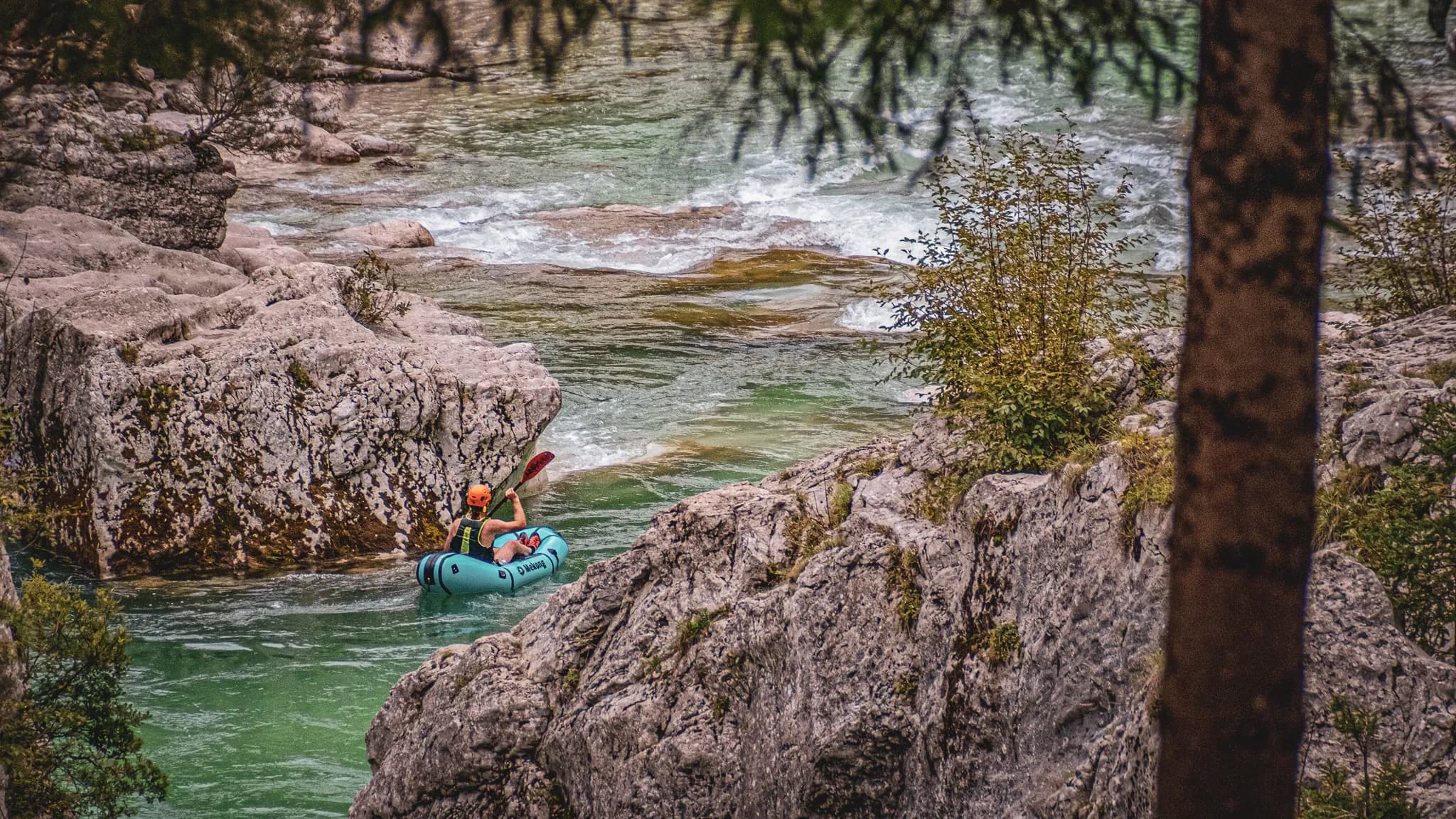 Un aventurier glisse paisiblement sur une rivière alpine, entouré de rochers et de verdure.