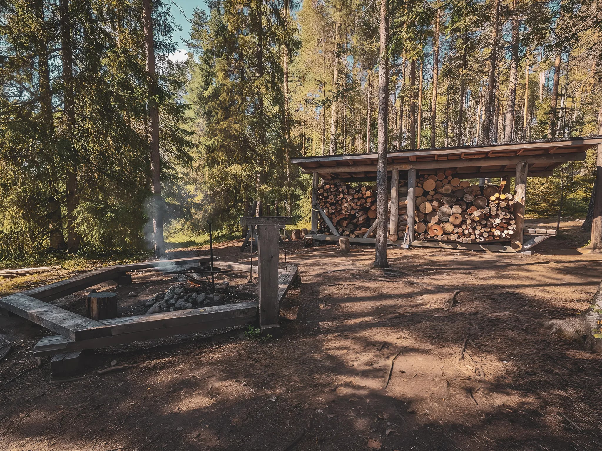 Wooden shelter in the heart of a forest in Lapland, with a campfire and stacked wood.