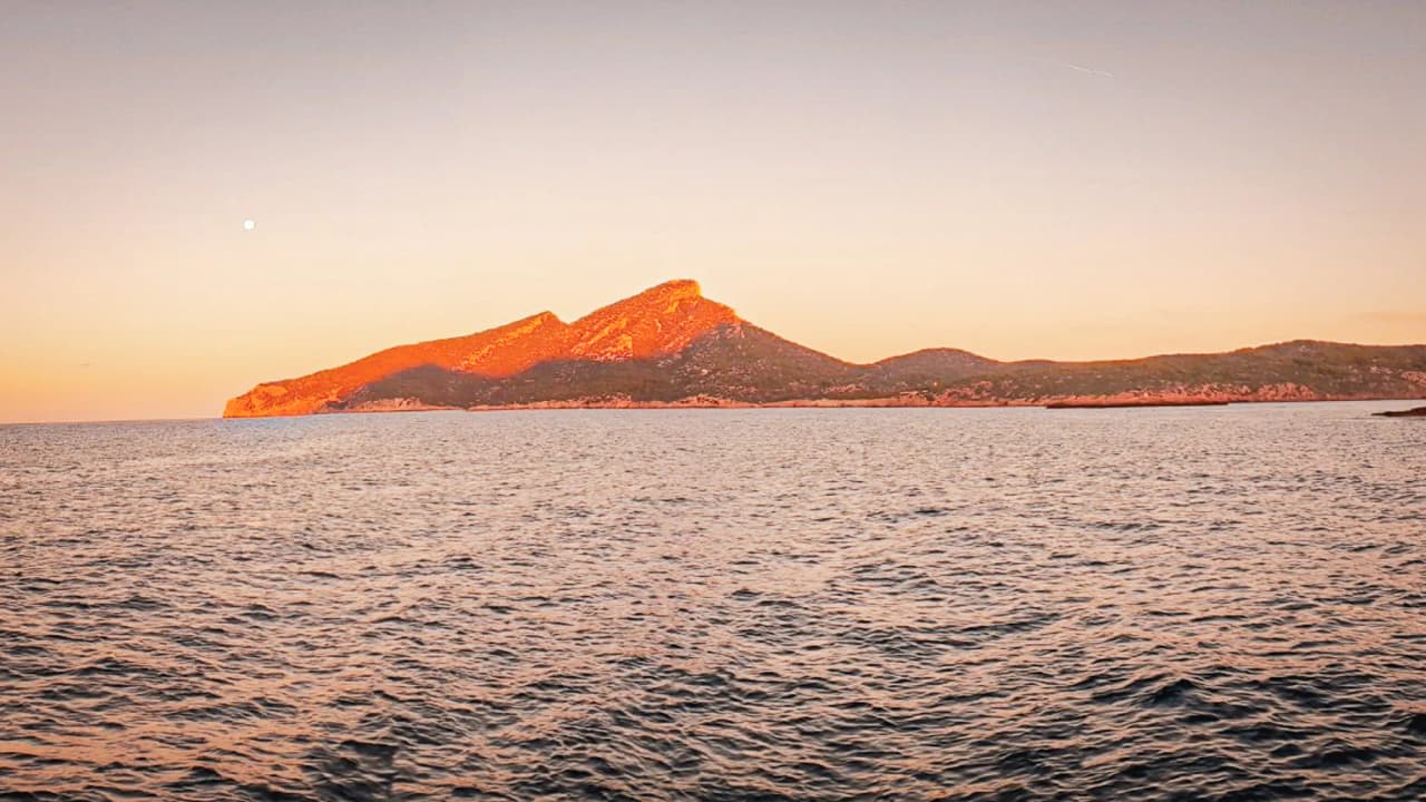 Sunset over the Balearic mountains, seen through calm waters.