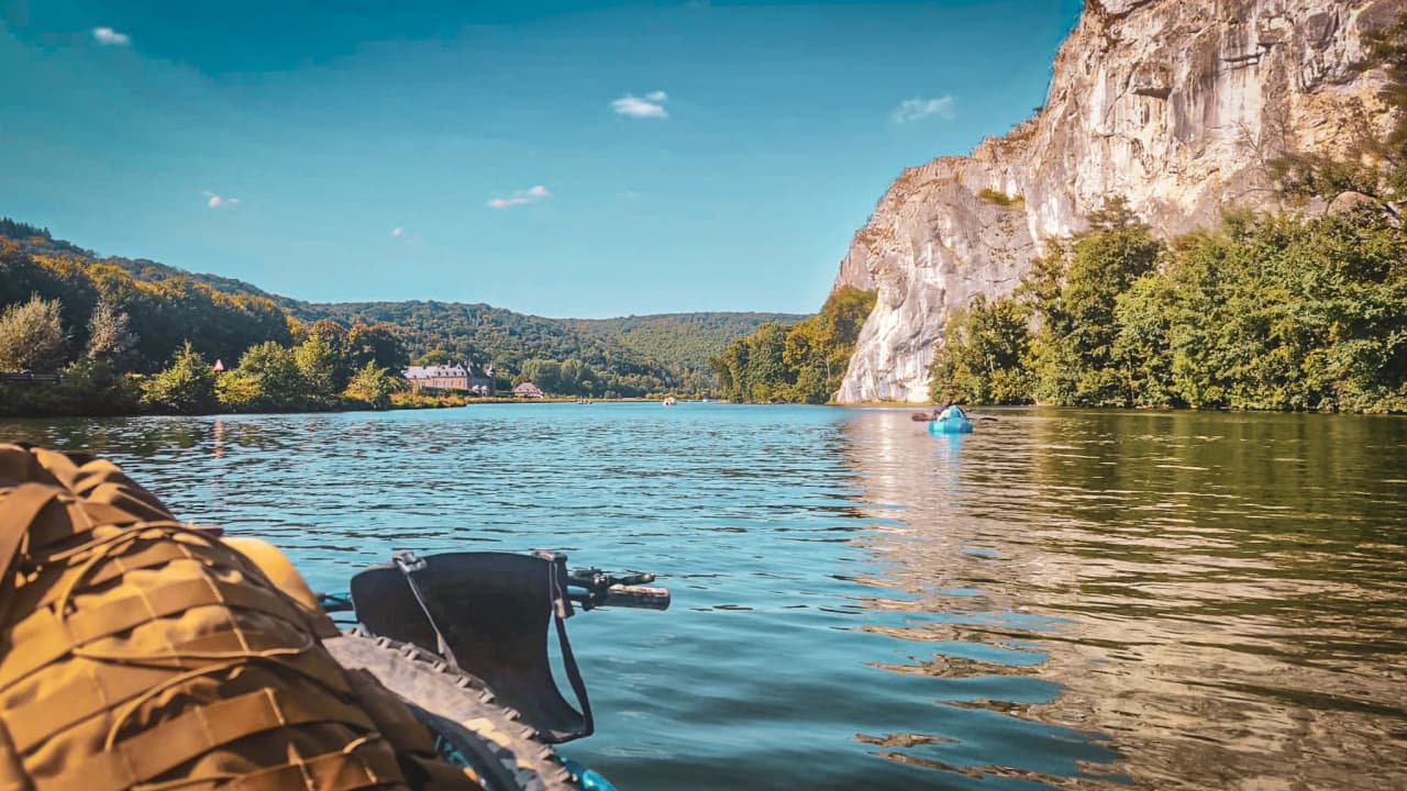 A peaceful river surrounded by cliffs and greenery, a packraft adventure in the Lesse valley.