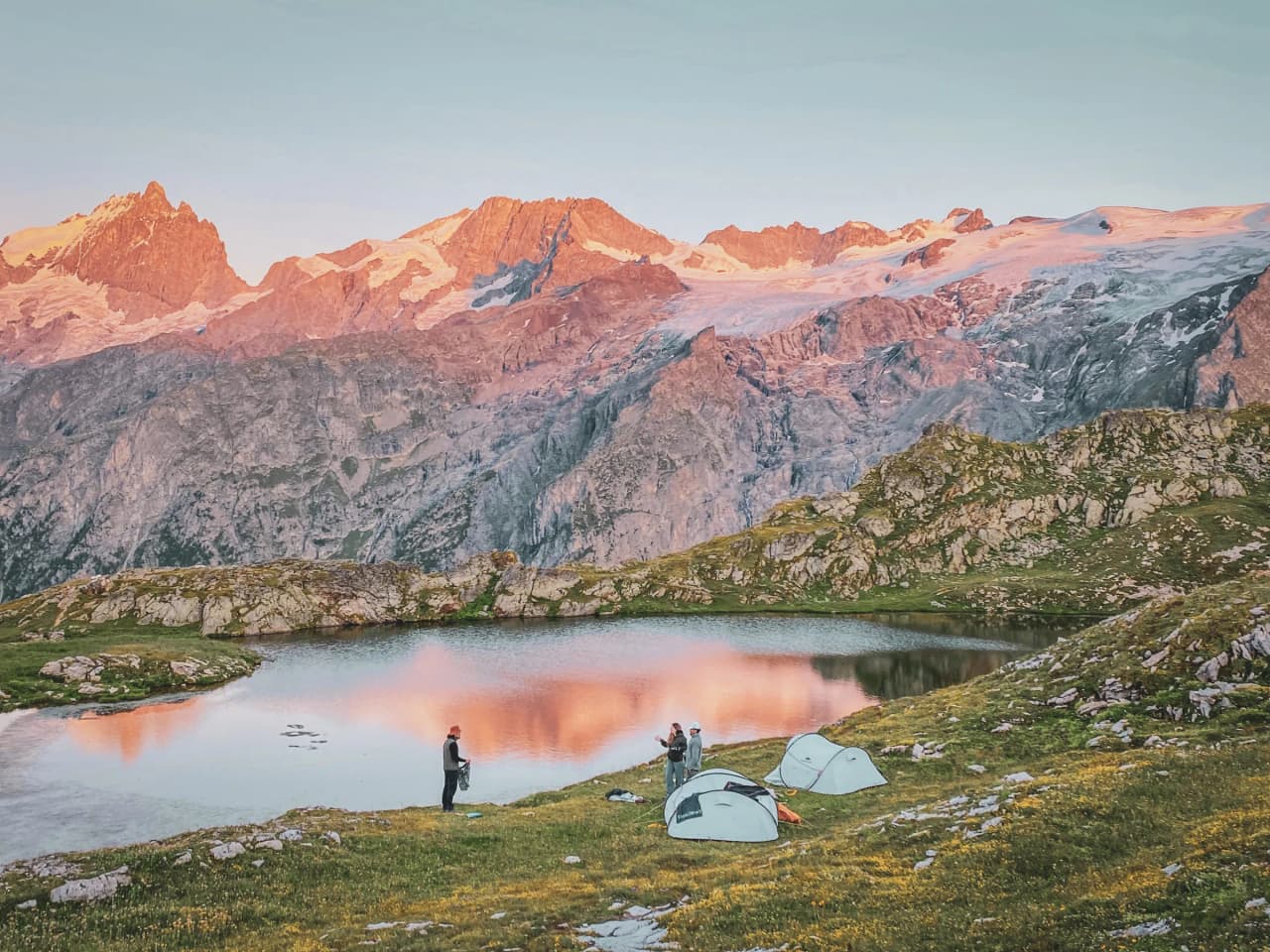 Un bivouac enchanteur au bord d'un lac, entouré de sommets majestueux illuminés par le coucher de soleil.