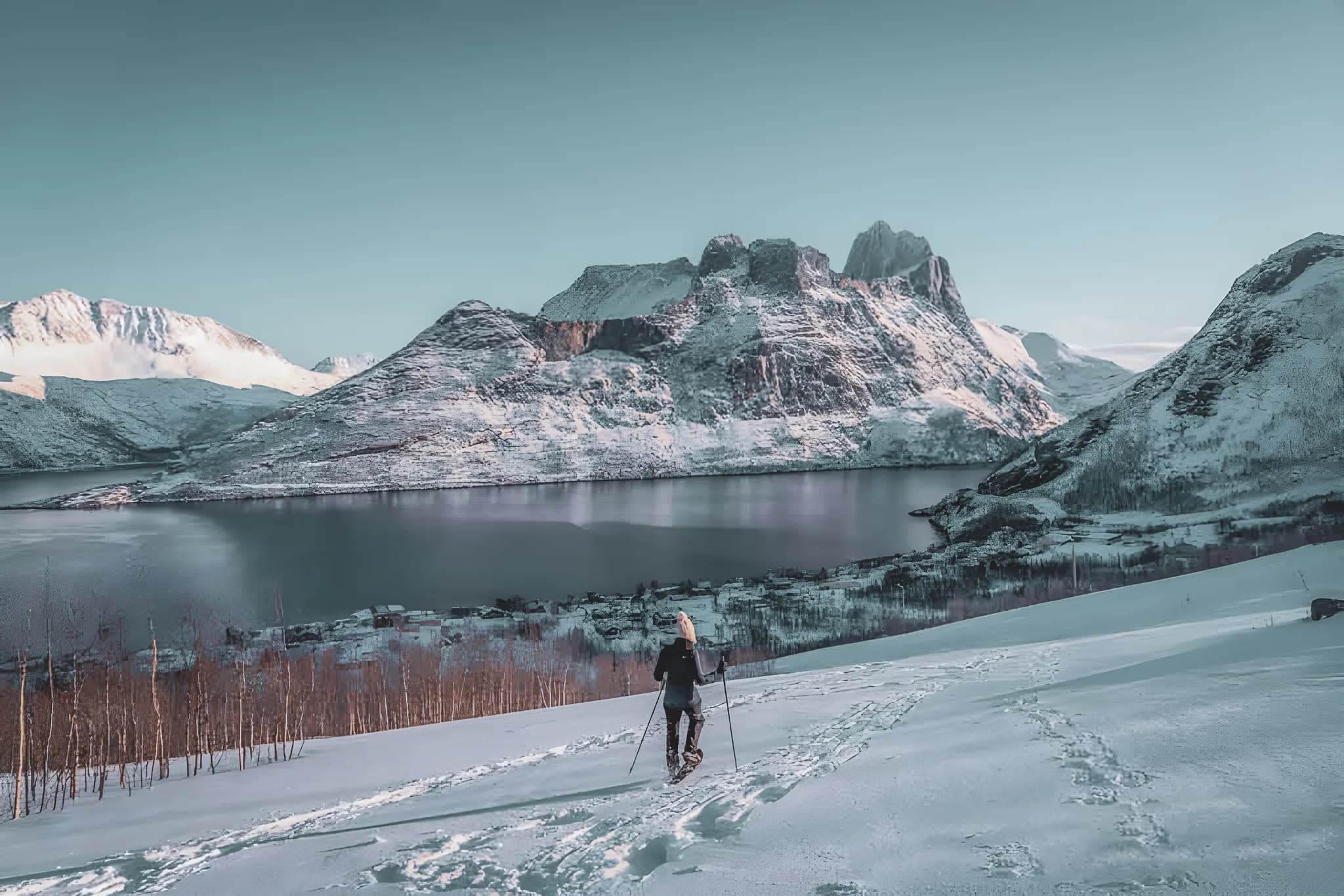 Sneeuwschoenwandelaar op een besneeuwd fjordenlandschap in Senja, Noorwegen, onder een serene hemel.