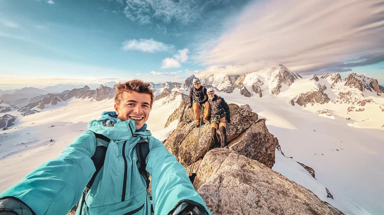 A group of smiling mountaineers on the summit of Mont Blanc, surrounded by majestic scenery.