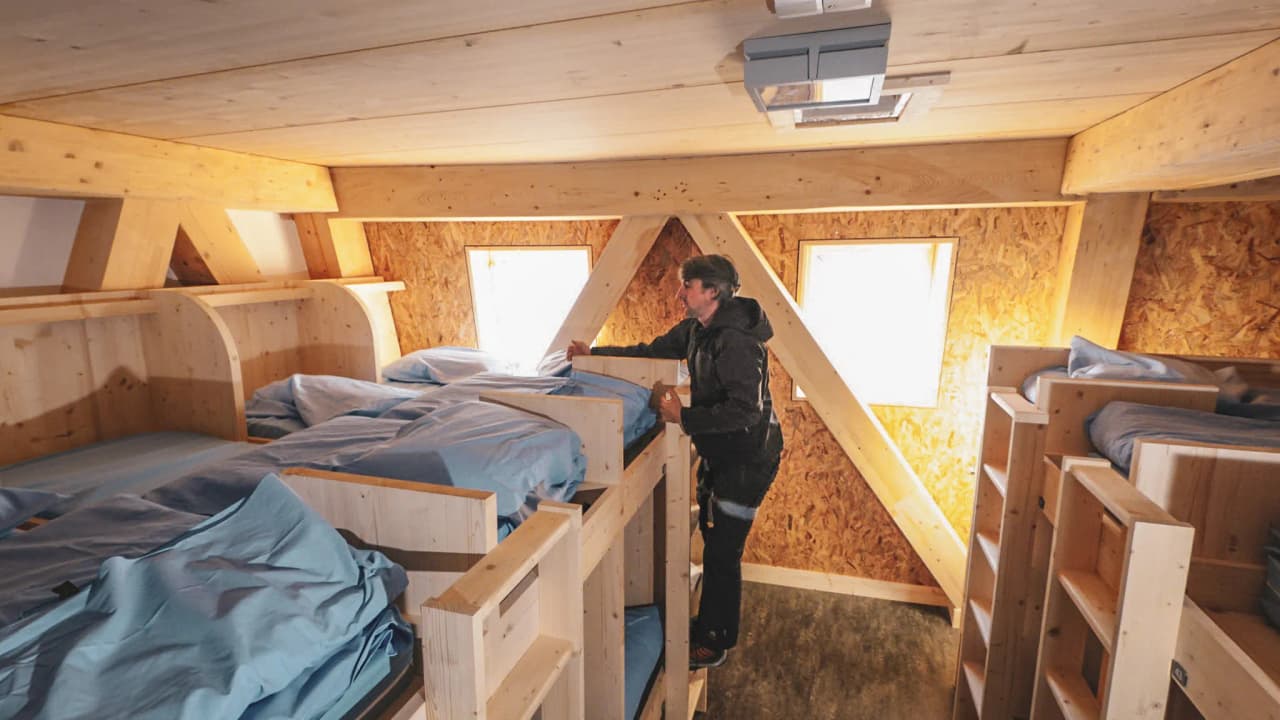 Een bergbeklimmer schikt zijn bed in een heldere Berghut, klaar voor avontuur.