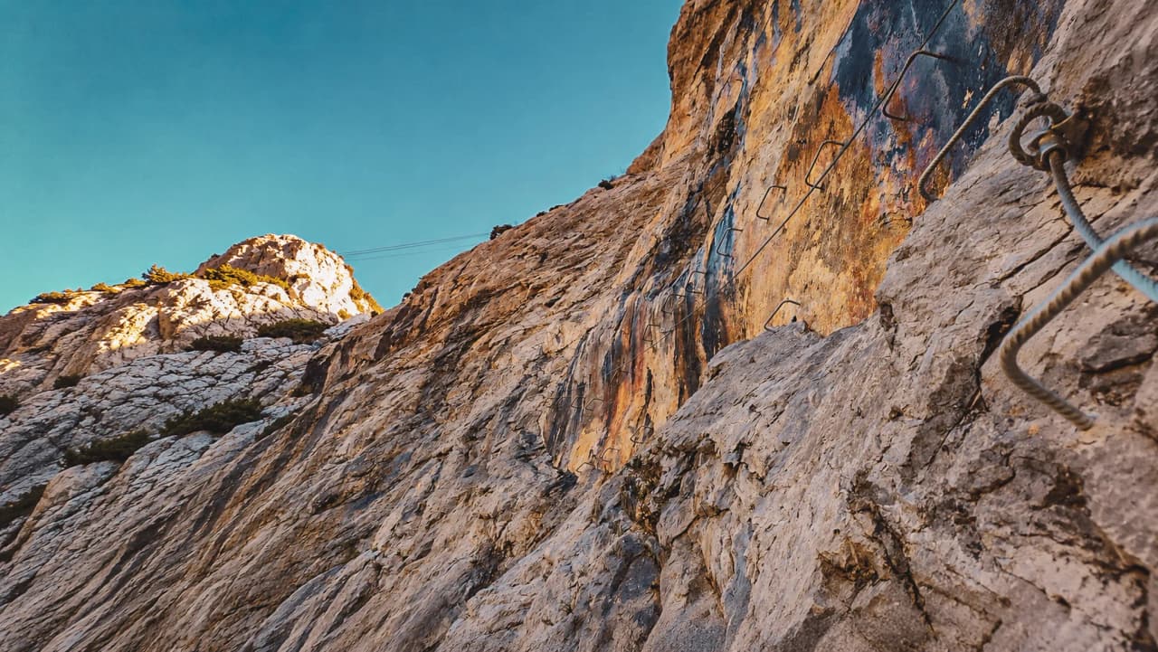 Mur rocheux avec échelles pour via ferrata, sous un ciel bleu, invitant à l’aventure.
