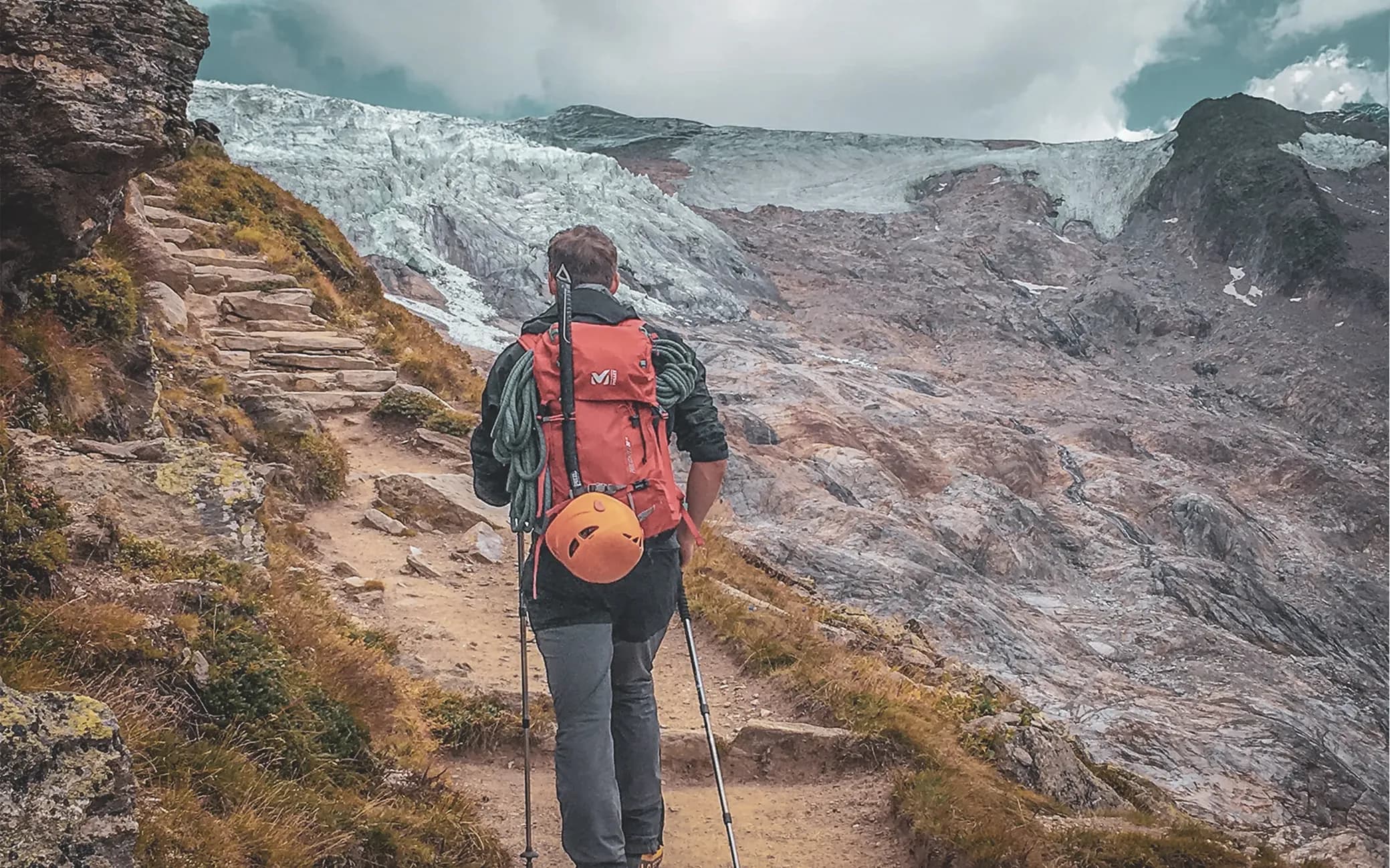 A climber on a mountain path, with a glacier in the background, ready for adventure.